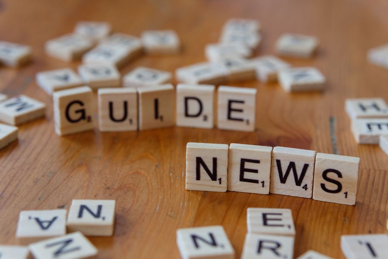 Close-up of Scrabble tiles spelling 'Guide' and 'News' on a wooden surface.