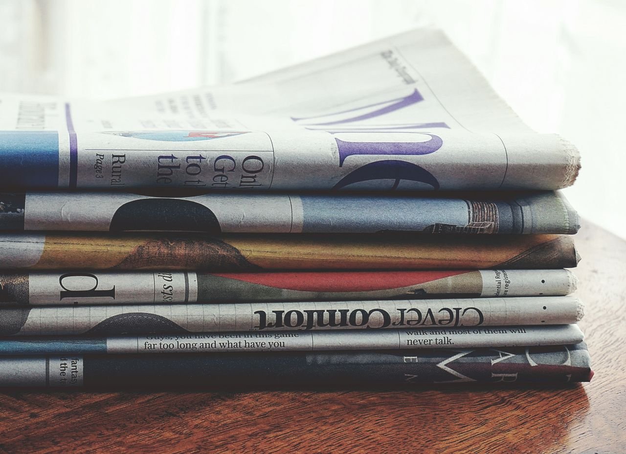 A stack of folded newspapers placed on a wooden table, symbolizing news and information.